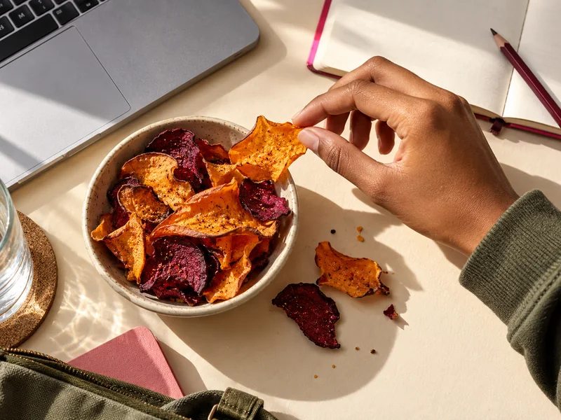 Snack break at a desk: a hand takes a crisp from a bowl beside a laptop and notebook